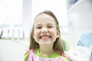 Relaxed little girl showing her healthy milk teeth at dental office, smiling and waiting for a checkup. Early prevention, paedodontics and no fear concept.
