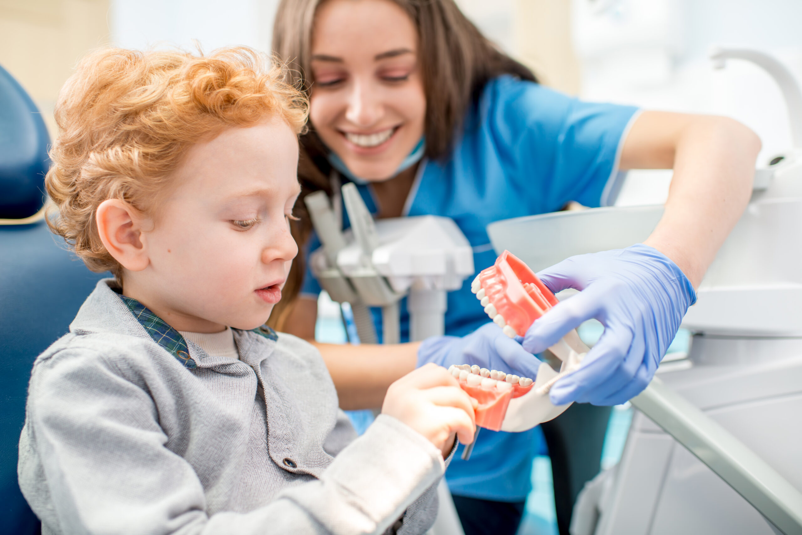 Female pediatric dentist showing a young boy a model jaw at the dental office