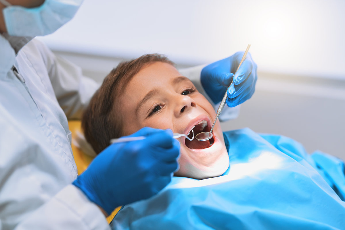 Shot of a young little boy lying down on a dentist chair while getting a checkup from the dentist.